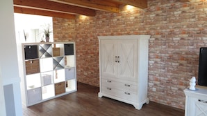 Een kamer met een bakstenen muur, houten balken, een witte kast met lades en een plank met manden.