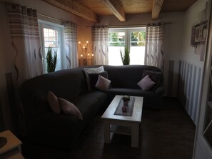 Uma sala de estar acolhedora com um sofá de cor escura, uma mesinha branca e uma janela com cortinas.