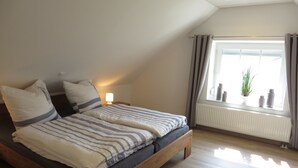 Een slaapkamer met twee bedden, een raam met gordijnen, een radiator en een bedlampje.