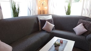 Een moderne woonkamer met een grijze hoekbank, een houten salontafel met een vaas en kaarsen, en een decoratieve lamp.