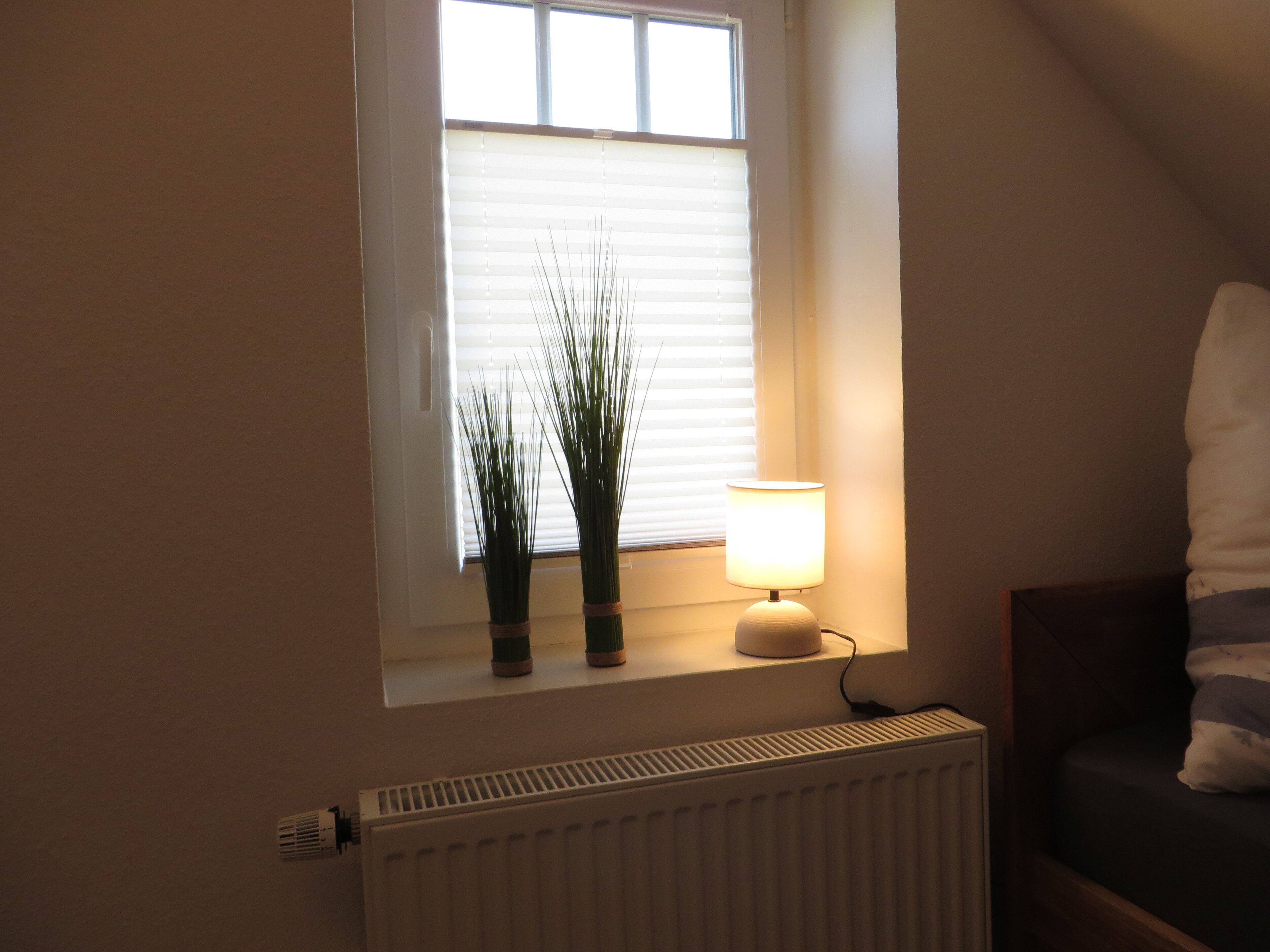 Une pièce avec une fenêtre, un radiateur et une lampe sur une table.