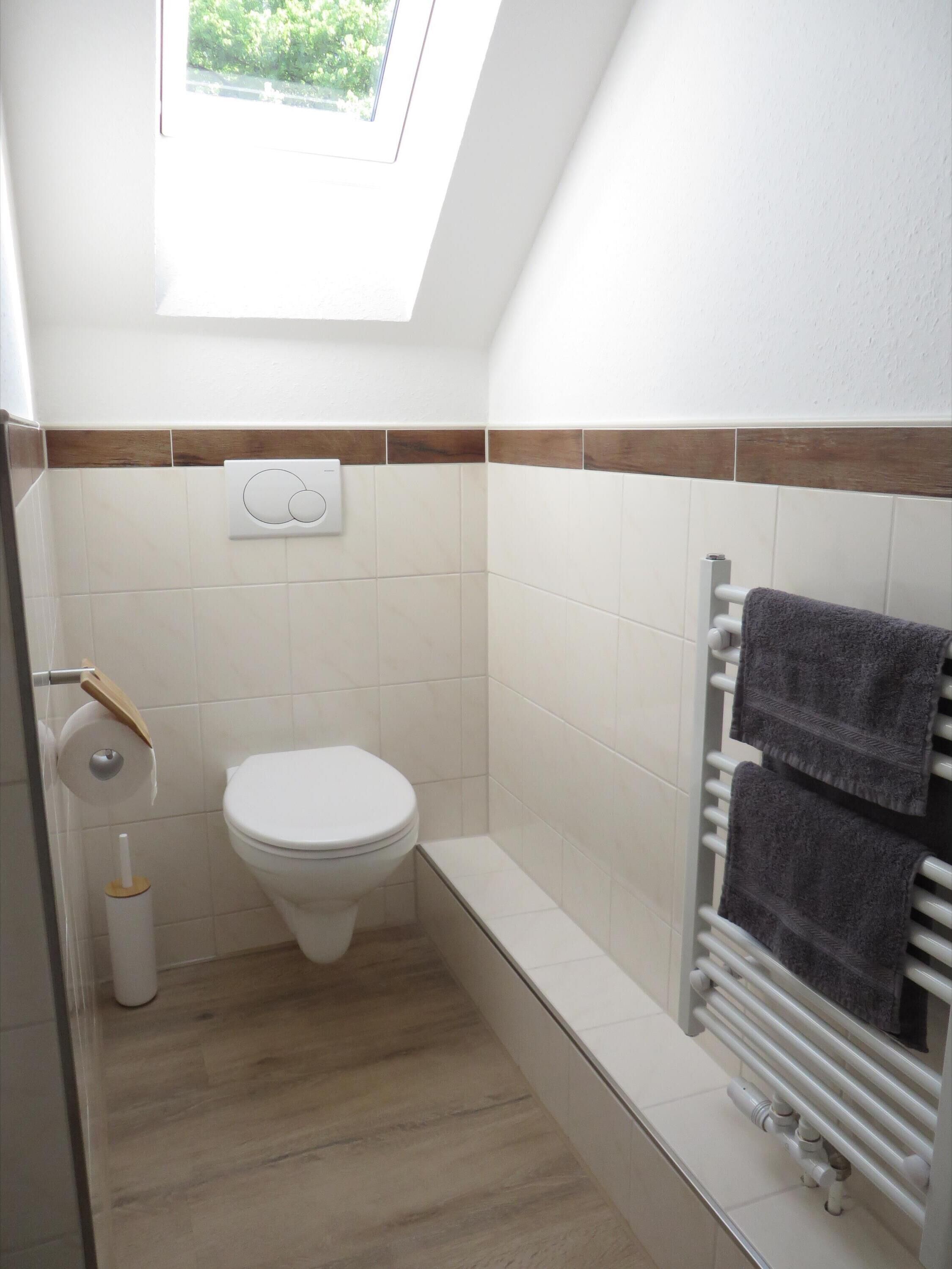 A small, modern bathroom with a toilet, a towel rack with two towels, a toilet paper holder, and a radiator.