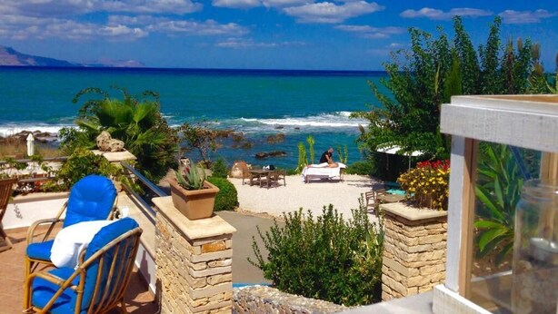 Une terrasse au bord de la plage avec vue sur l’océan, une chaise longue et une table où une personne se détend.