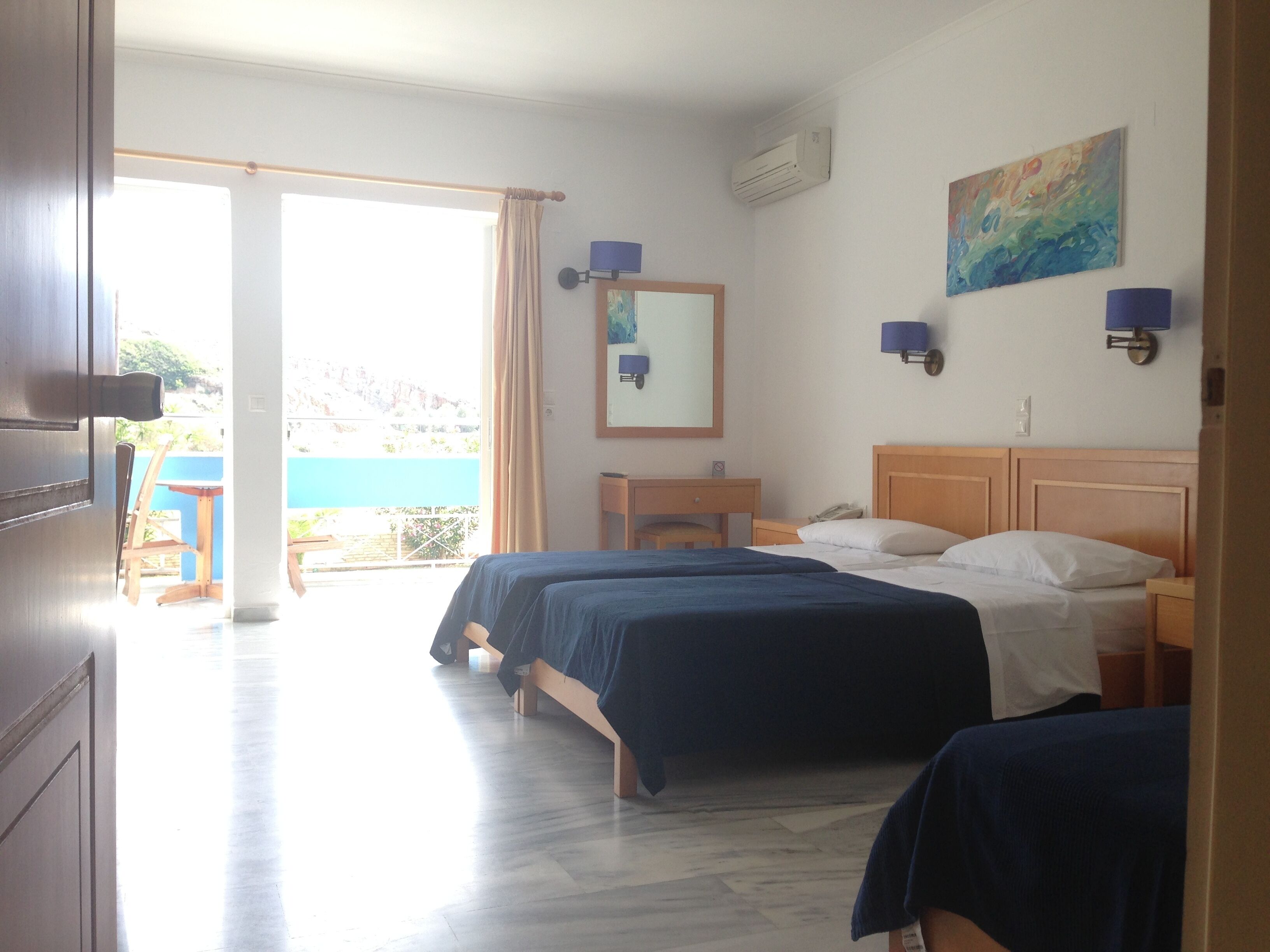 A hotel room with two beds, a wooden headboard, a small bedside table, a nightstand, a mirror, and a painting on the wall.