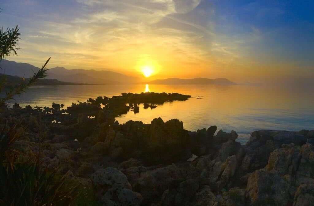 Un atardecer sobre una costa rocosa con agua tranquila que refleja el cielo.