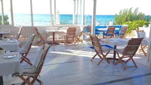 Une pièce baignée de lumière naturelle, avec vue sur l’océan, meublée de chaises et de tables en bois, et dotée d’un petit espace piscine.
