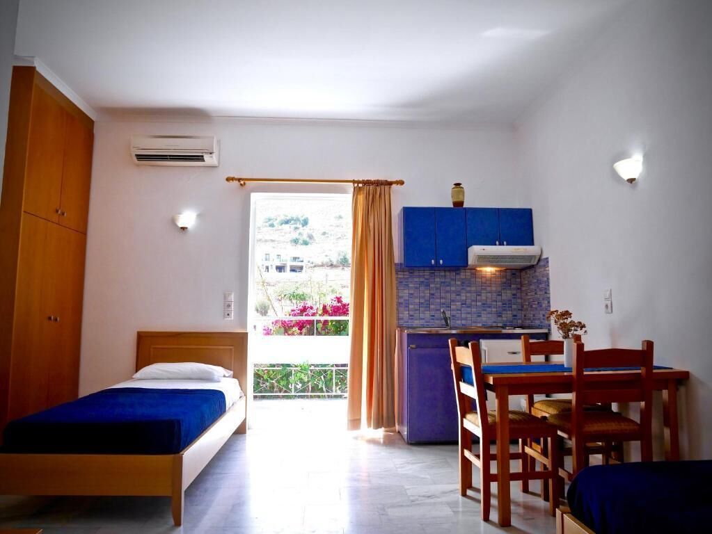 A bedroom with a bed, a wooden wardrobe, and a small kitchenette with a blue cabinet and a stove.