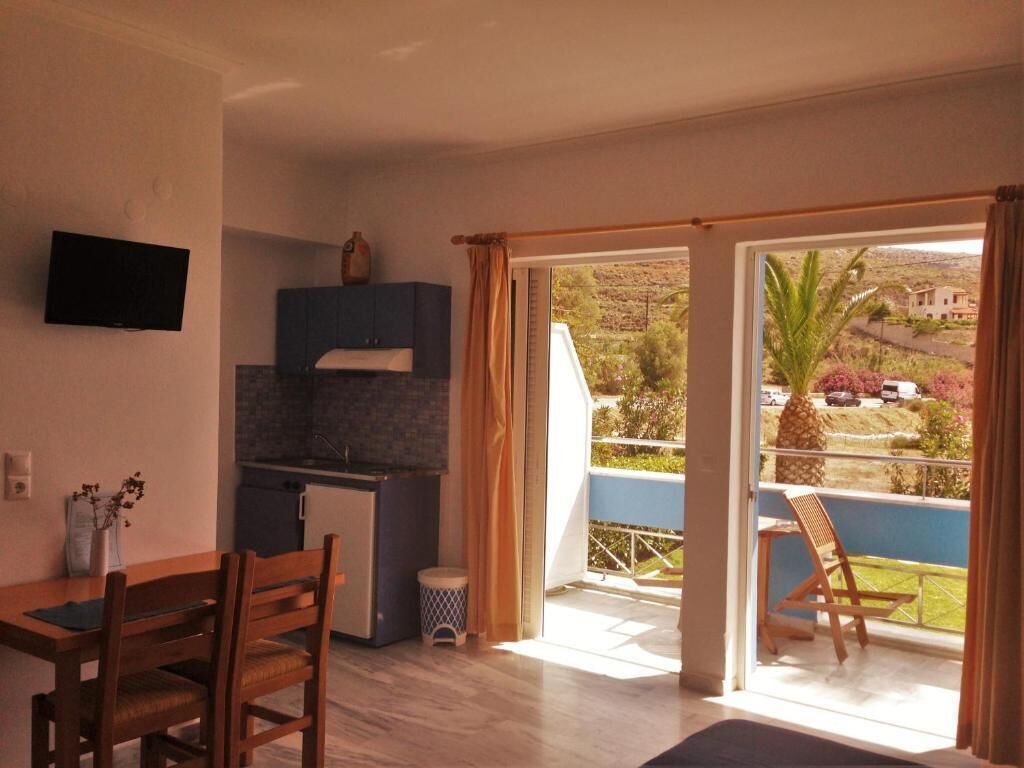 A modern kitchen with a flat-screen TV, a dining area with wooden furniture, and a balcony with a view of the surrounding landscape.