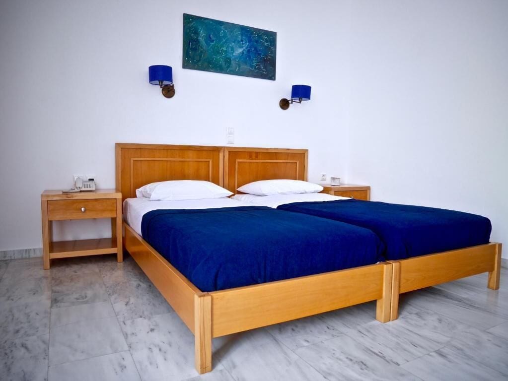 A double bed with a wooden frame and blue bedding, two bedside tables, and a wall-mounted lamp.