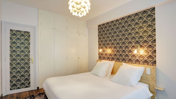 A bedroom with a bed, white wardrobe, patterned wallpaper, and a unique ceiling light fixture. - Superior apartment, 400m from the Palais des Festivals (Cannes)