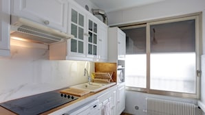 A modern kitchen with white cabinets, a built-in stove, and a window with blinds. - Superior apartment, 400m from the Palais des Festivals (Cannes)