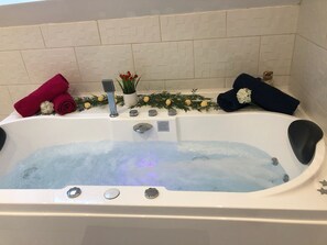 A bathtub with water, a showerhead, and a control panel. There are towels and a plant on the edge.