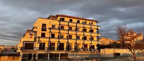 A multi-story building with balconies, located near a waterfront.