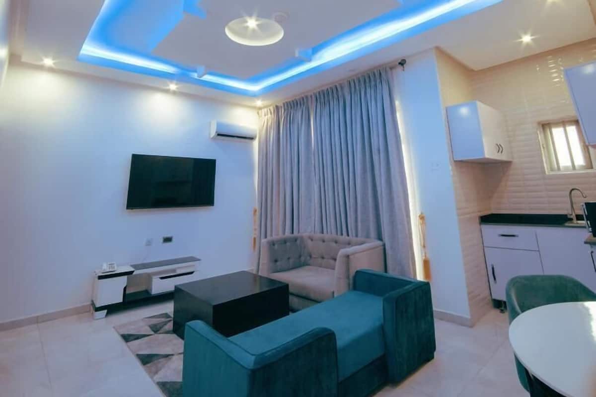 A modern living room with a flat-screen TV, a sofa, a coffee table, and a dining area with a table and chairs.