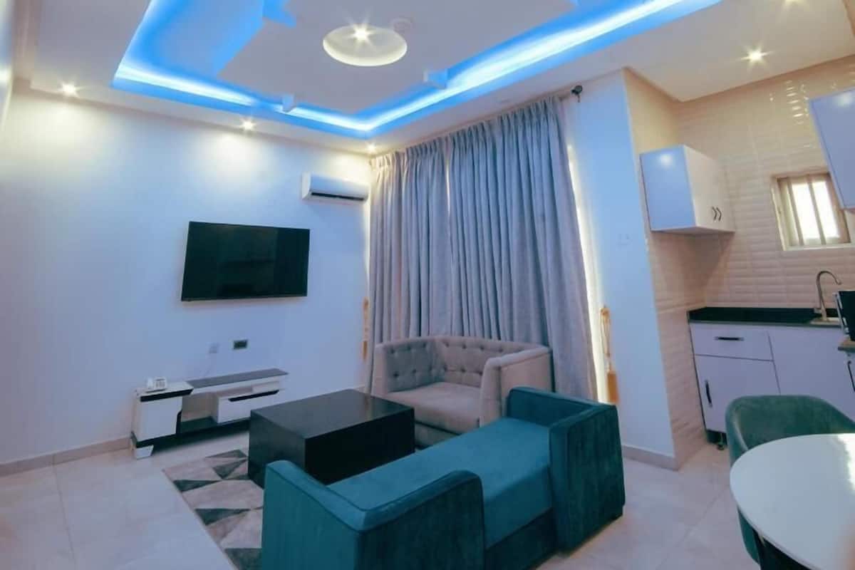 A modern living room with a flat-screen TV, a sofa, a coffee table, and a dining area with a table and chairs.