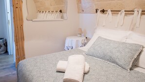A bedroom with a bed, pillows, a towel, a small table with a lamp, and a wall-mounted towel rack.