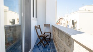 A balcony with two wooden chairs, a white wall, and a view of buildings.