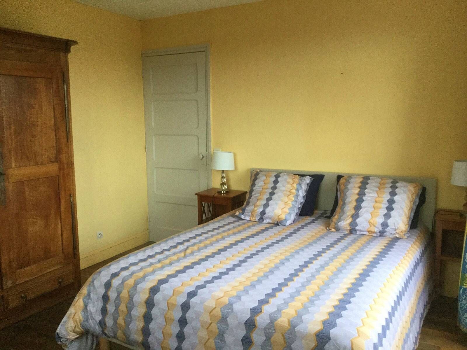 A bedroom with a bed, two bedside tables, a wooden wardrobe, and a door.