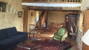 Um interior rústico com um quarto no mezanino, uma área de refeições e uma sala de estar mobiliada com móveis de estilo vintage.