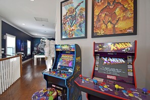 Una habitación con dos máquinas de videojuegos arcade, una de Marvel Super Heroes y otra de X-Men, y un póster de Captain Marvel en la pared.