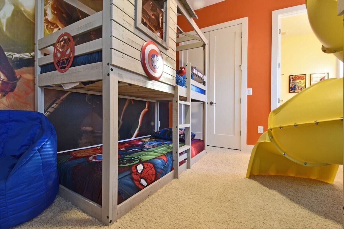 A bunk bed with a Spider-Man themed bedspread, a yellow slide, and a door in the background.
