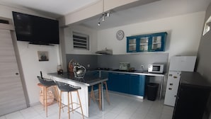 A compact kitchen with a central island, blue cabinets, a microwave, and a TV mounted on the wall. - Cosy F2 in cosy villa + car rental possible (Pointe noire)