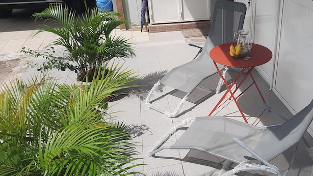 A patio area with two clear plastic lounge chairs and a small red table with a glass top. - Cosy F2 in cosy villa + car rental possible (Pointe noire)
