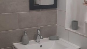 A bathroom with a white sink, two faucets, a mirror, and a window with blinds. - Cosy F2 in cosy villa + car rental possible (Pointe noire)