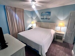 Ein Hotelzimmer mit einem Bett, zwei Nachttischen mit Lampen, einem Deckenventilator, einem Bild an der Wand und einer Tür.