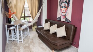 Un salon moderne avec un canapé en cuir marron, une table à manger en bois avec des bancs, un hamac et un grand tableau abstrait accroché au mur.