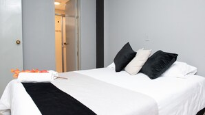 Un lit bien fait, avec une literie blanche et noire, un plaid noir et un bouquet de fleurs orange.