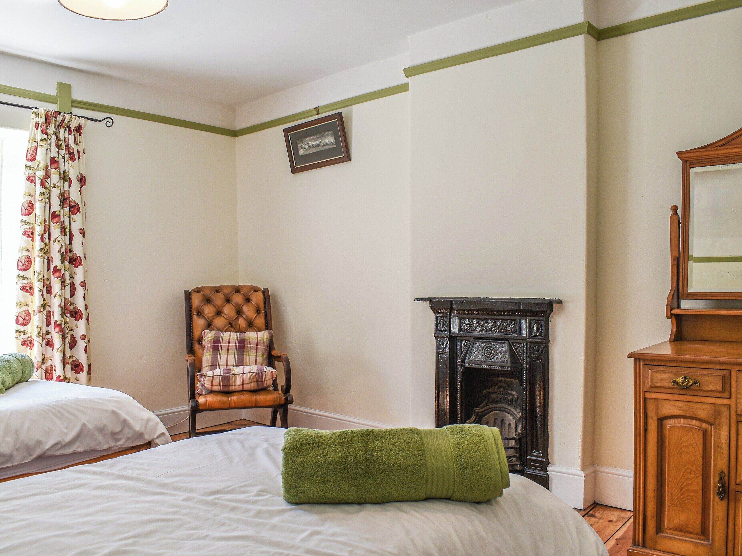 A bedroom with a bed, a chair, a fireplace, and a wooden cabinet.