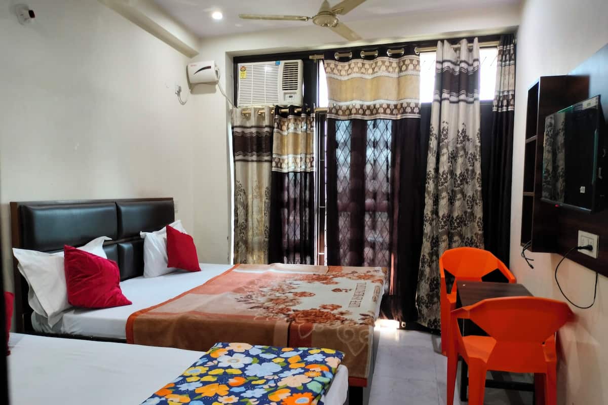 A hotel room with two beds, a desk, an orange chair, a TV, and an air conditioning unit.