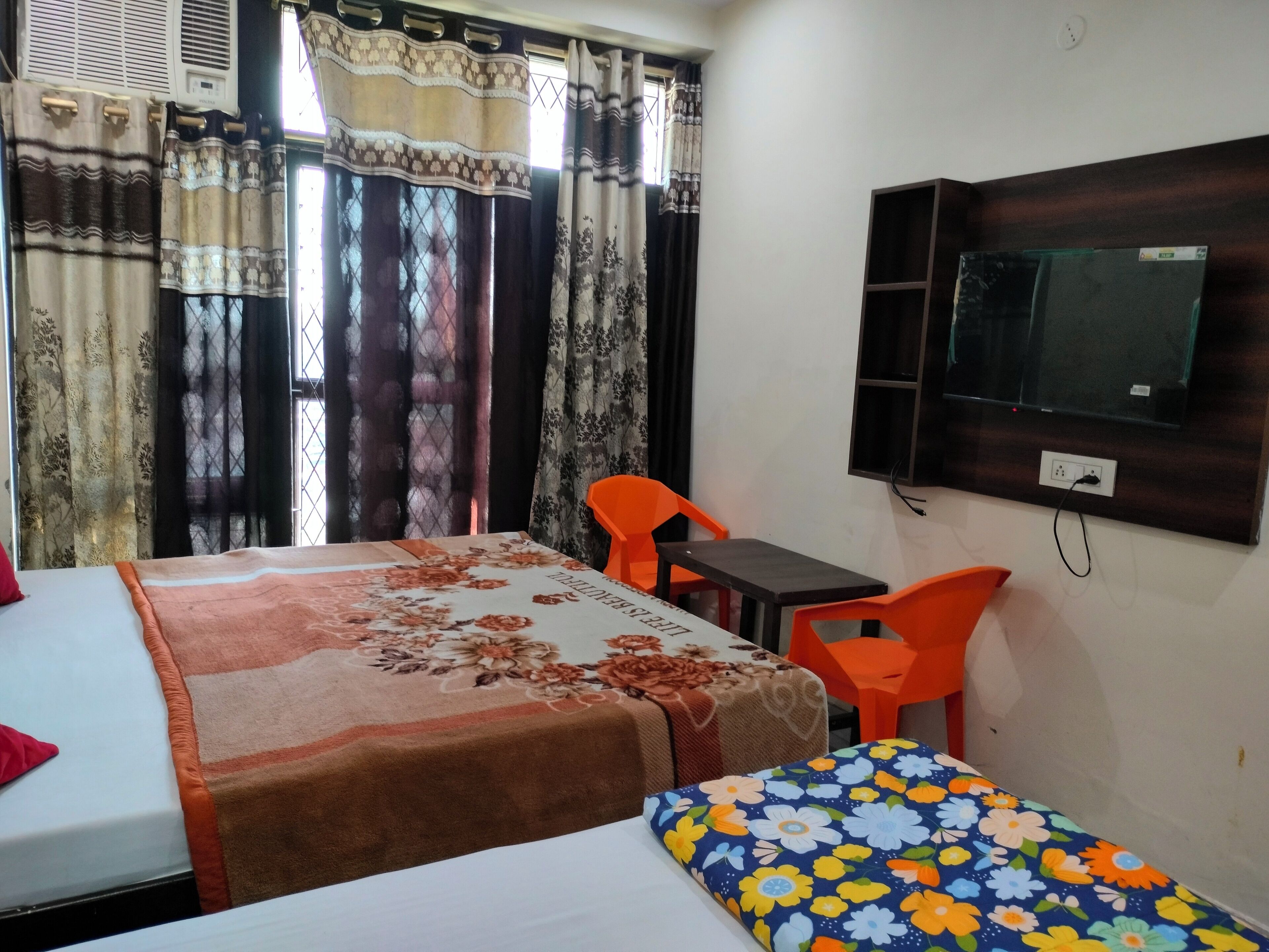 A room with two beds, a TV, and orange chairs.