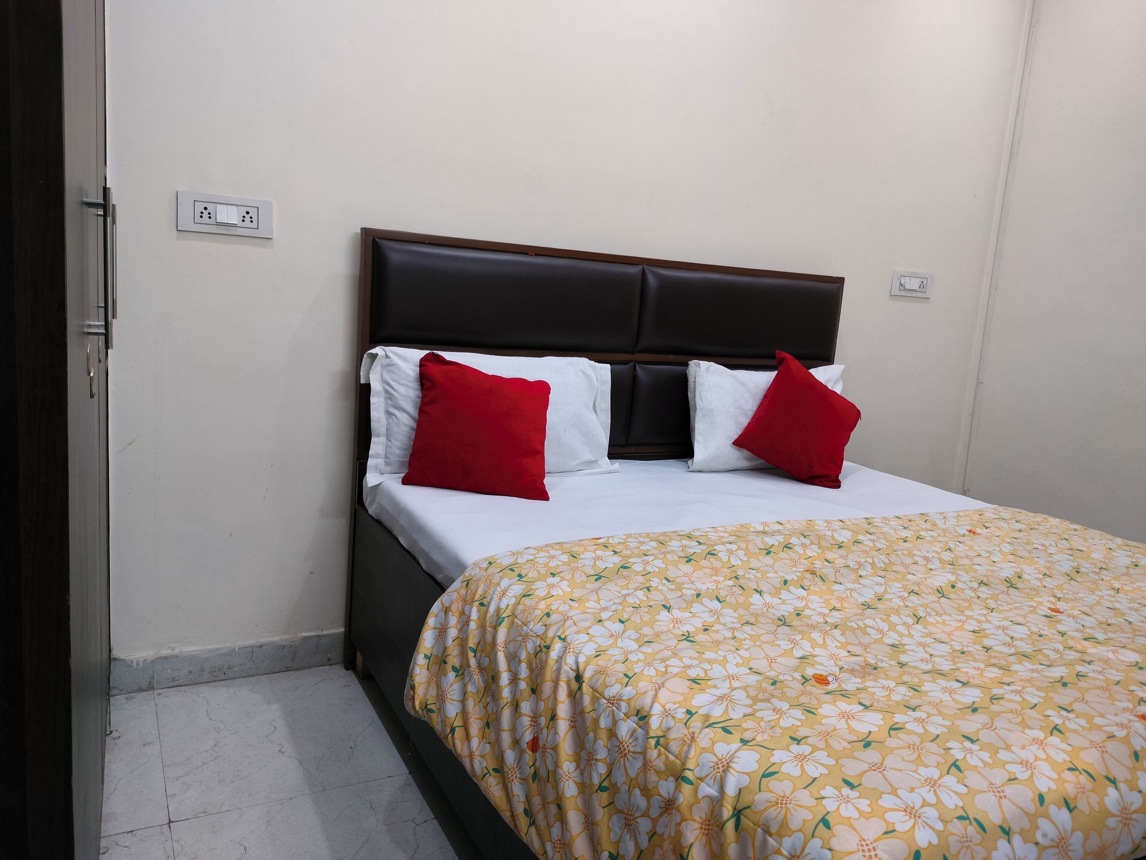 A neatly made bed with a floral bedspread, a dark headboard, and two red pillows.