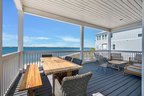 A wooden deck with a table and chairs, overlooking a body of water.