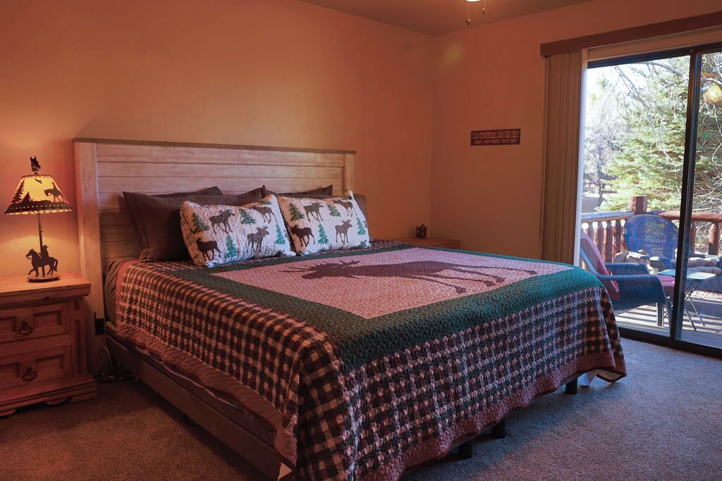 A bedroom with a large bed, a nightstand, a lamp, and a view of the outdoors through a sliding glass door.