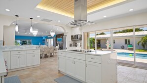 A modern kitchen with white cabinets, a central island, and a view of a swimming pool. - Exquisite Courtyard Villa on St. Thomas East End / Ocean Views + Modern Comfort (St Thomas)