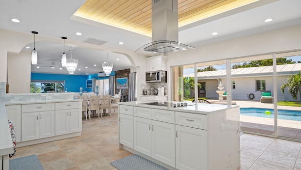A modern kitchen with white cabinets, a central island, and a view of a swimming pool. - Exquisite Courtyard Villa on St. Thomas East End / Ocean Views + Modern Comfort (St Thomas)