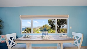 A dining area with a table set for two, a window with a view of the outdoors, and a blue wall. - Exquisite Courtyard Villa on St. Thomas East End / Ocean Views + Modern Comfort (St Thomas)