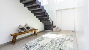 Een moderne trap met een geometrisch ontwerp, een houten bank met kussens, en een kamerbreed tapijt in een lichte, ruime kamer.