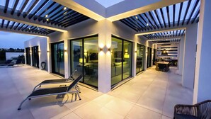 Een modern buitenterras met glazen deuren, een lounge stoel en een eethoek.