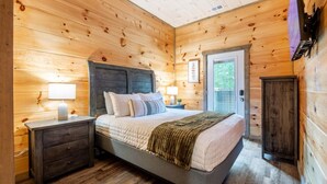 Une chambre aux murs lambrissés, comprenant un lit, des tables de chevet, une commode et une porte donnant sur l’extérieur.