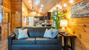 L’intérieur d’une cabane en rondins, avec un canapé en cuir noir, des murs en bois, un coin cuisine et une table à manger.