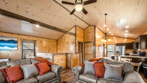 Un intérieur de chalet chaleureux avec deux canapés en cuir, un plafond en bois et un coin cuisine.