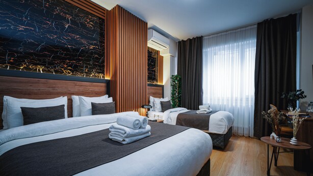 Ein Hotelzimmer mit zwei Betten, einem großen Fenster mit Vorhängen, einem Holz-Kopfstück und einer Wand-Klimaanlage.