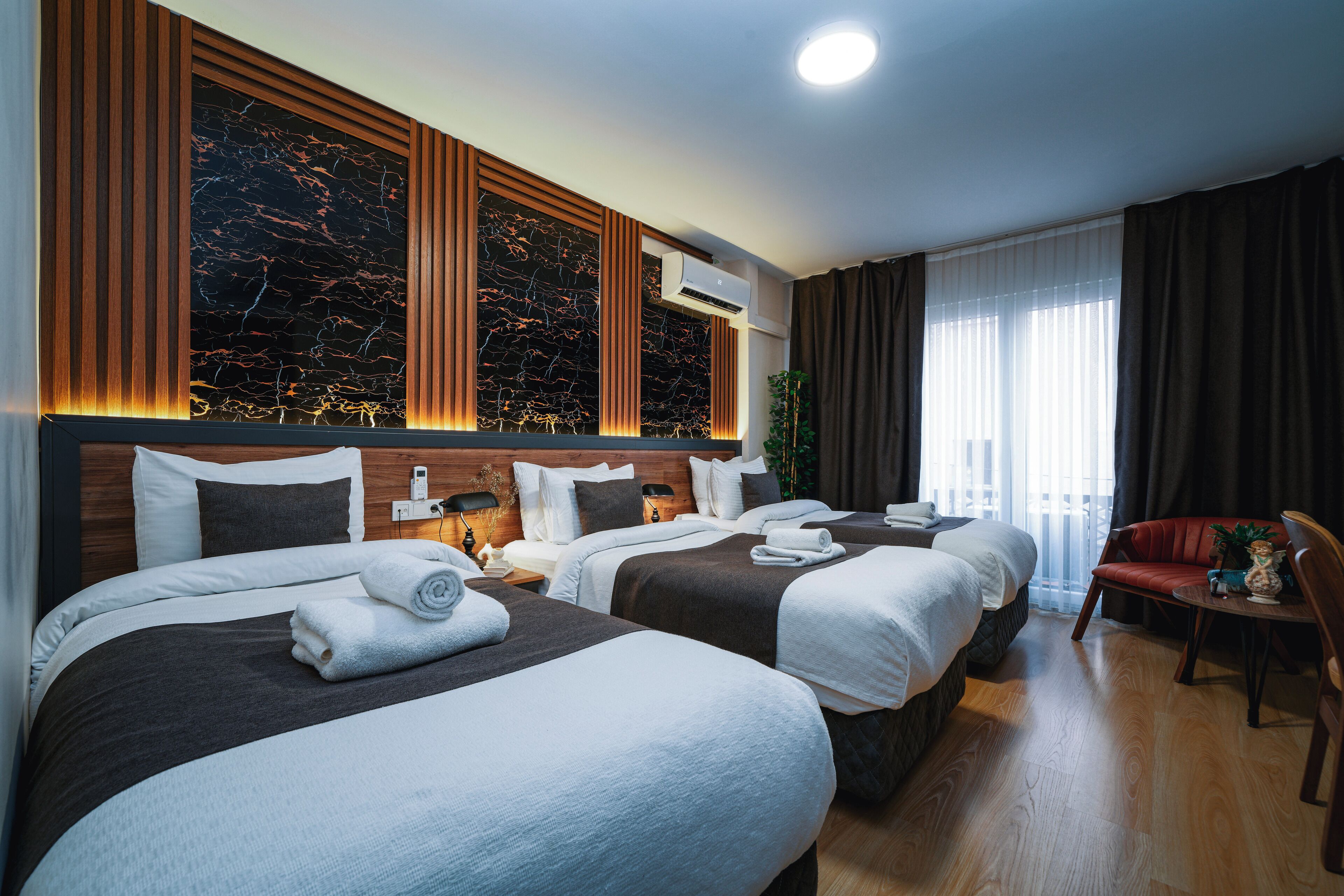 A hotel room with three beds, a wooden headboard, a marble wall, and a large window with curtains.