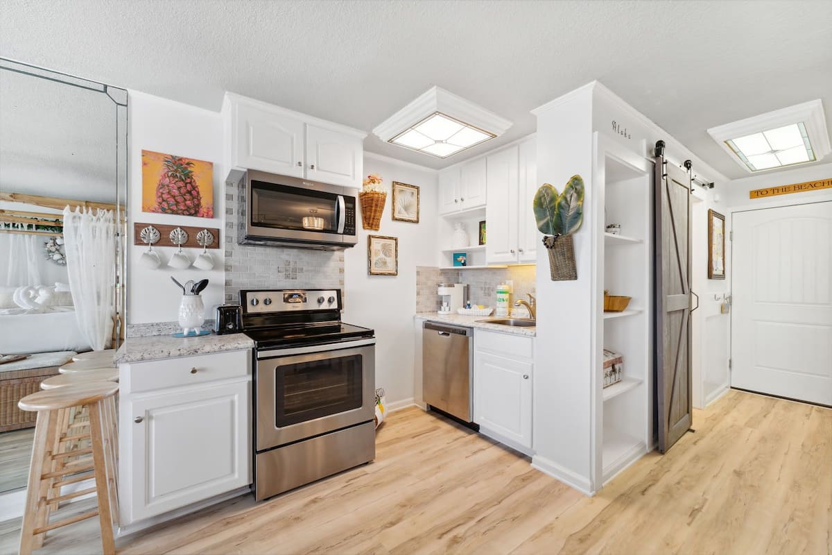 A modern kitchen with white cabinets, stainless steel appliances, and a wooden floor.