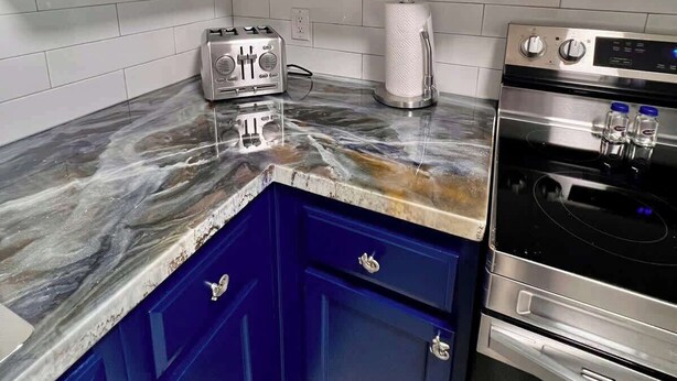 A kitchen with white cabinets, a marble countertop, a toaster, a paper towel dispenser, and a stainless steel oven.