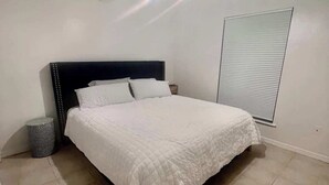 A bedroom with a bed, a bedside table, a lamp, and a window with blinds.